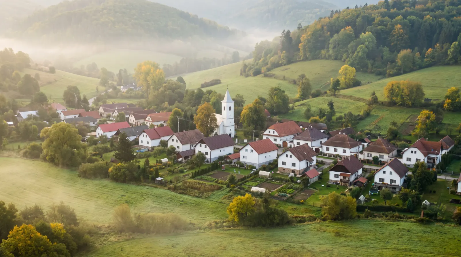 Pohľad na Javorovce z lúk nad obcou, uprostred biela veža kostola, za obcou zalesnené kopce