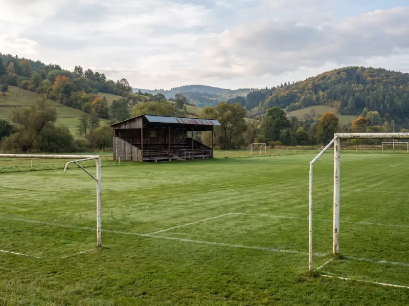 Futbalové ihrisko s drevenou tribúnou pod zalesnenými kopcami